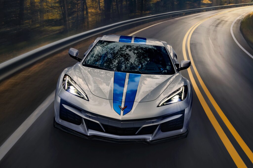 GM Is Promising Hybrids Again, So Why Does It Rub Me the Wrong Way? Chevrolet E-Ray coupe, in silver paint with blue racing stripes, races around a bend.