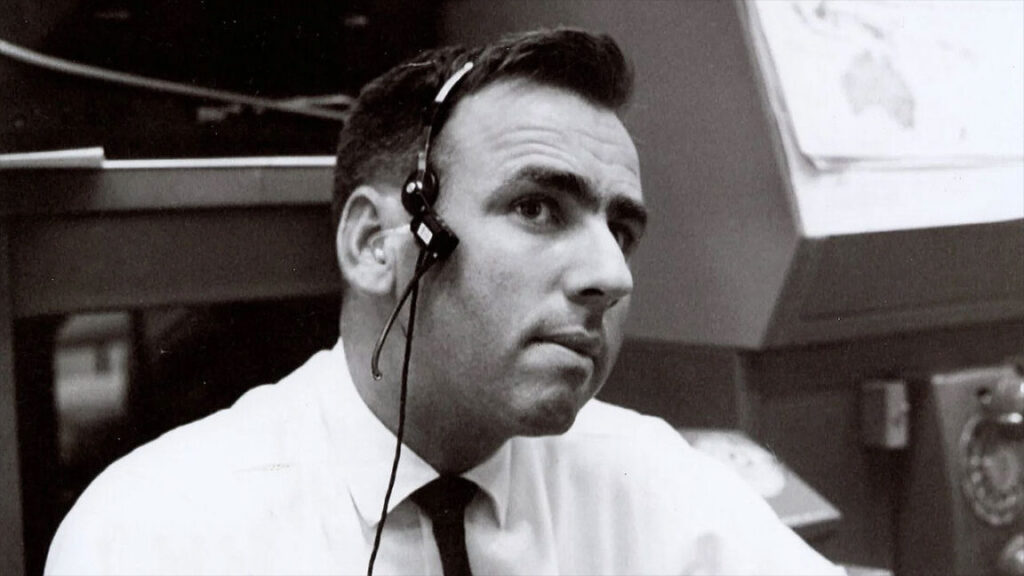 Milt Windler, NASA flight director who helped save Apollo 13, dies at 94 a black and white photo of a man in a white button-down shirt and thin black tie wearing a headset while seated in a room