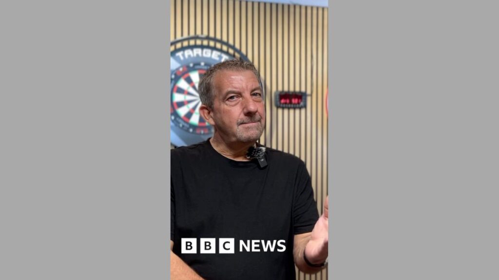 New vape tax makes Bracknell store add dart boards to its stock A man wearing a black t-shirt, stood in front of a wooden wall with a darts board behind him