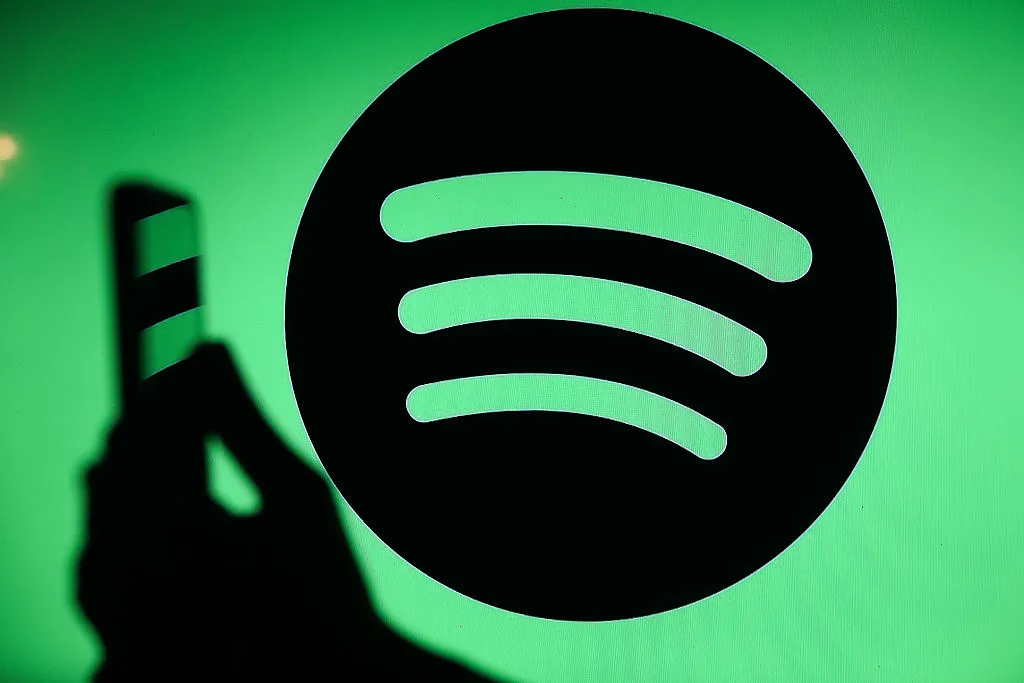 Spotify expands audiobooks to over 180 markets The Spotify logo displays on a screen with a person holding a phone.